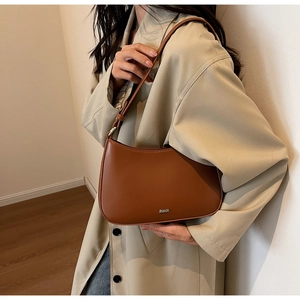 Detail of caramel leather shoulder bag with metallic logo on a trench coat outfit