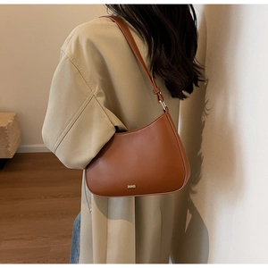 Brown leather crescent bag with gold logo shown on model's shoulder in modern setting