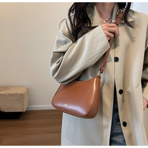 Close-up of vintage brown leather baguette bag with elegant golden hardware on model