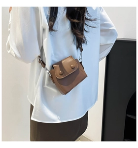 Close-up of a brown mini crossbody bag with double buckles on a white outfit