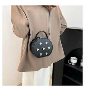 Détail d'un sac bandoulière rond noir mat avec rivets argentés et bandoulière métal