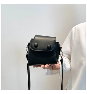 Detail of minimalist black mini flap crossbody bag with decorative buckles and matte finish