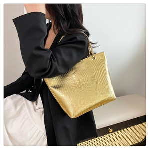 Détail d'un sac cabas doré avec texture crocodile et chaîne en métal sur modèle
