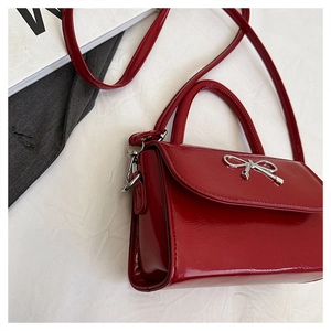 Detail of red patent leather handbag featuring a silver metal bow and flap closure