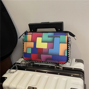 Modische Kettentasche mit bunten Tetris-Mustern auf einem weißen Koffer liegend