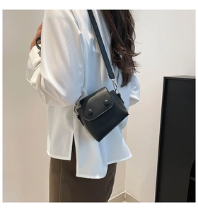 Detail of a black mini crossbody bag featuring dual round buckles and a slim shoulder strap