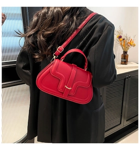 Detail of red litchi texture leather handbag with gold buckle on a model shoulder