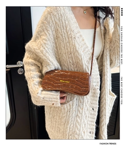 Detail of a brown crocodile pattern shoulder bag with Miss mini text on a beige sweater
