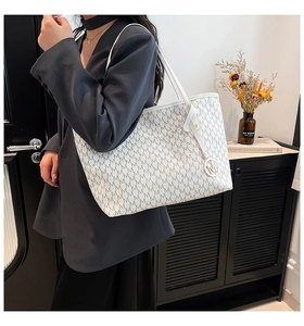 Makroaufnahme der weißen Shopper-Tasche mit M-Muster und metallischem Logo-Anhänger