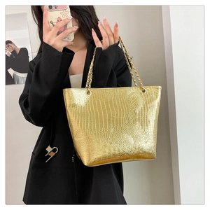 Golden tote bag featuring faux crocodile texture and dual metal chain straps shown on person