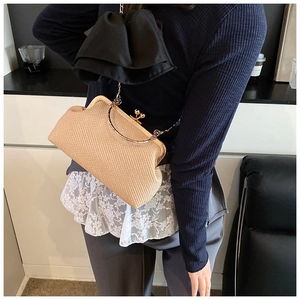 Detail of straw woven crossbody bag featuring a large black satin bow and metal chain