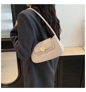 Close-up of golden heart-shaped lock on cream leather shoulder bag worn by model