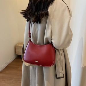 Minimalist red leather crescent underarm bag with gold logo on beige trench coat