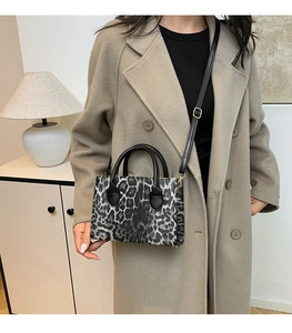 Chic leopard print handbag with black circular handles and adjustable strap on a beige coat