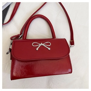Detail view of glossy dark red leather handbag with a silver metal bow accent
