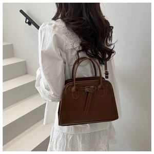 Sac Boston marron foncé avec ceinture, porté par un mannequin sur un escalier blanc