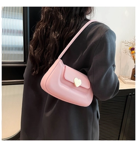 Close-up of pink crossbody bag with metal heart buckle worn by model from behind
