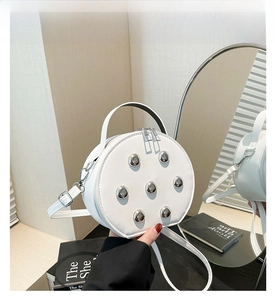 Detail of white round crossbody bag featuring silver stud accents and dual zippers