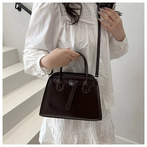 Detail of dark brown tote bag on white stairs featuring unique strap buckle design