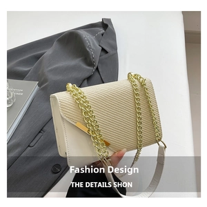 Detail of white woven crossbody bag featuring a chunky gold chain strap and metal trim