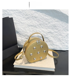 Detail of round gold PU leather crossbody bag with silver rivets and dual zipper closure