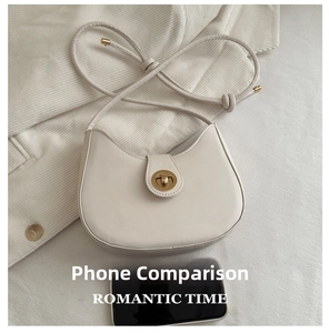 Detail of a creamy white half-moon bag with gold lock next to a smartphone for size scale