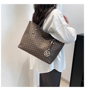Model trägt eine große dunkelbraune Tragetasche mit M-Monogramm und Silberanhänger