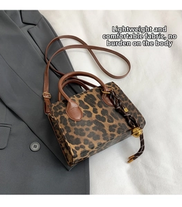 Detail view of leopard print tote bag with brown handles and a decorative bell charm