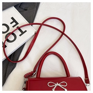 Flat lay of a red glossy patent leather handbag with a silver metal bow buckle detail