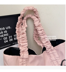 Detail of soft pleated handles on a pink nylon tote bag showing durable stitching