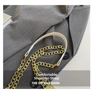 Close-up of the elegant gold metal chain strap on a creamy white faux leather handbag