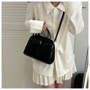 Sac trapèze noir brillant avec boucle argentée porté sur une jupe plissée blanche élégante