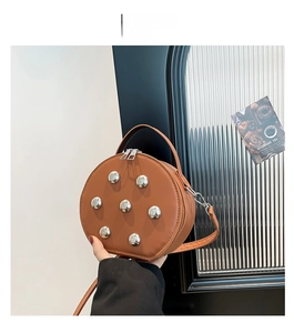 Detail view of round tan leather crossbody bag with silver studs and chain strap