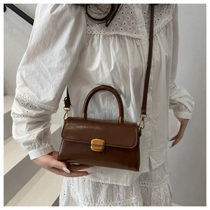 Sac bandoulière vintage marron en similicuir avec boucle dorée porté par un mannequin