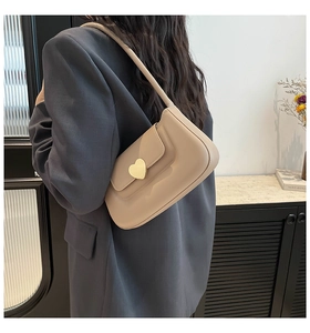 Dettaglio di una borsa sottobraccio beige con fibbia a cuore indossata come borsa a spalla
