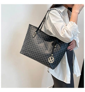 Detailed shot of dark grey canvas tote with leather straps and metal M pendant on model