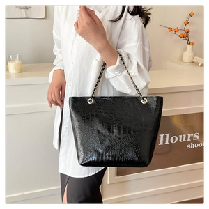 Detail of glossy black faux crocodile leather tote bag with elegant chain strap