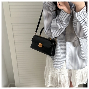 Détail d'un sac à main noir en cuir avec poignée dorée et serrure sur un modèle