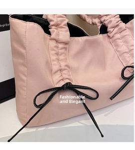 Close-up of pink pleated tote bag with black ribbon bow and textured cloud handle detail
