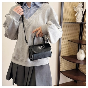 Detail of a black square PU leather bag with a silver bow clasp and adjustable strap