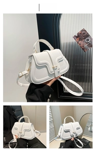 Detail of white saddle bag with wavy flap design and gold metal buckle on leather