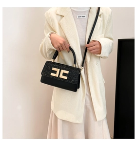 Détail d'un sac à bandoulière noir chic avec logo doré porté sur un blazer blanc