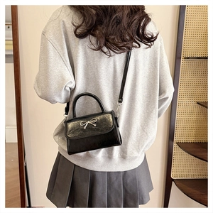 Model view of black glossy textured handbag with metal bow and detachable shoulder strap
