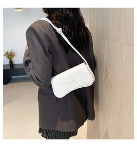 Close-up of white crocodile pattern baguette bag with gold logo and knotted strap detail