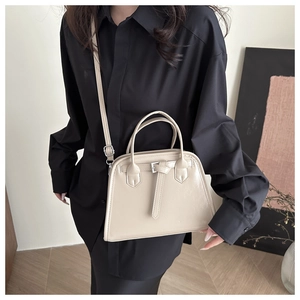 Gros plan d'un sac cabas beige en cuir avec poignées et bandoulière porté par un mannequin