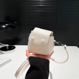 Mini cream white crossbody bag with decorative buckles shown in a modern office setting