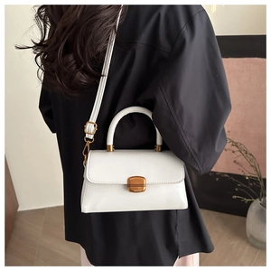 Détail d'un sac bandoulière blanc minimaliste avec boucles dorées et finition cuir lisse
