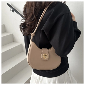 Détail du sac beige en forme de croissant avec fermoir doré et bandoulière à nœud décoratif