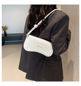 Close-up of a white crocodile embossed crescent shoulder bag worn by a model in a grey suit