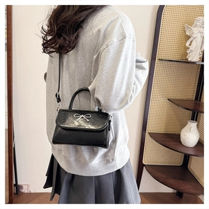 Elegant black handbag with silver bow detail shown on a model for size perspective